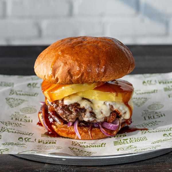 A juicy burger with melted cheese, pineapple, red onions, and BBQ sauce on a bun.