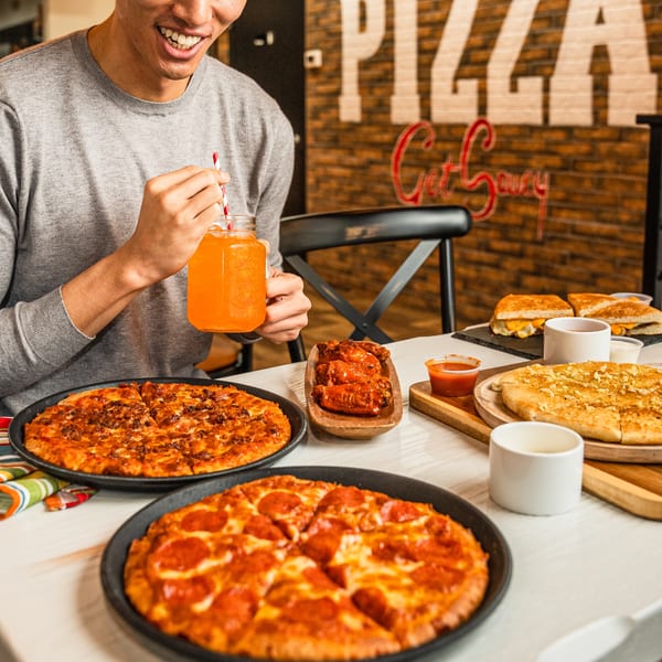 Smiling person enjoying pizza, wings, and a drink at Singas Famous Pizza.