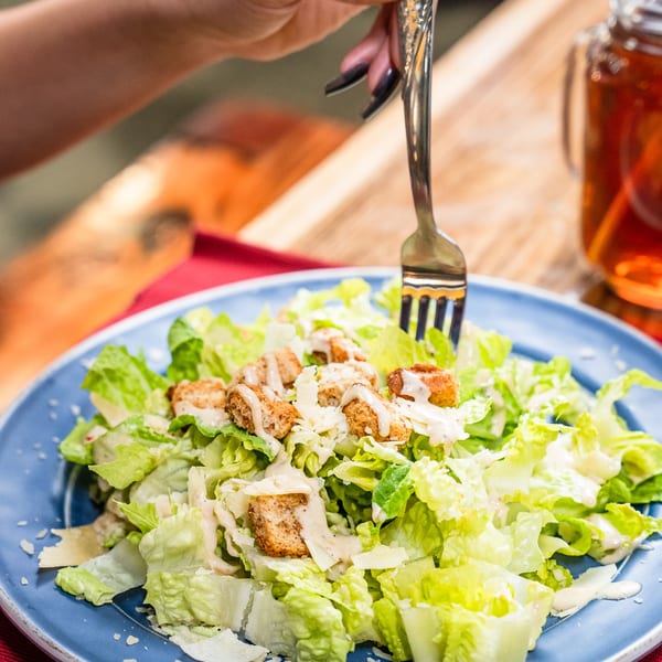 A person's hand with dark nail polish uses a fork to eat a fresh Caesar salad.