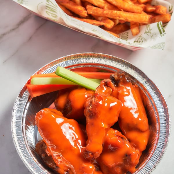 Singas Famous Pizza's buffalo wings with celery and carrots, alongside a basket of sweet potato fries.