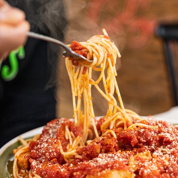Steaming spaghetti with red sauce and parmesan cheese being lifted by a fork.