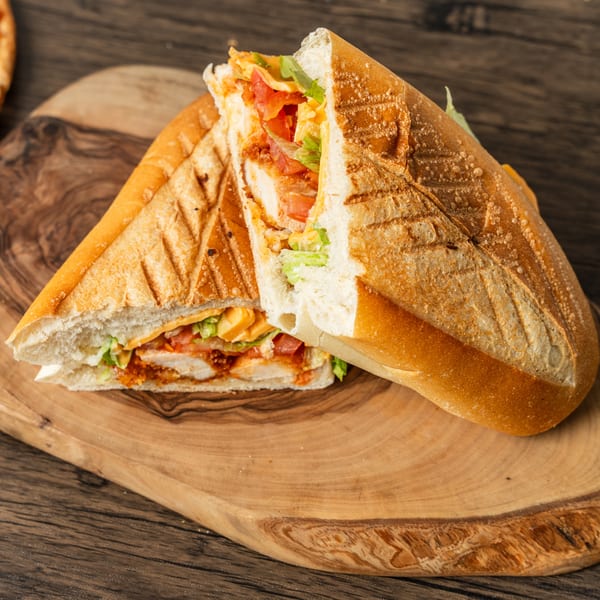 A toasted chicken sandwich with lettuce, tomato, and cheese, cut in half on a wooden board.