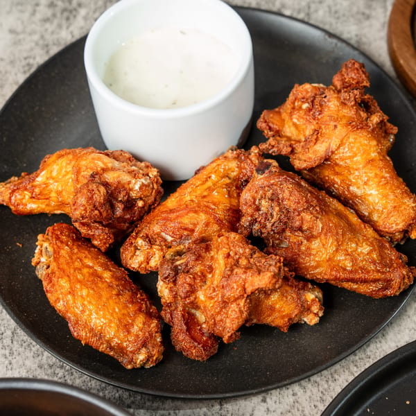 Crispy fried chicken wings with a side of creamy dipping sauce on a black plate.