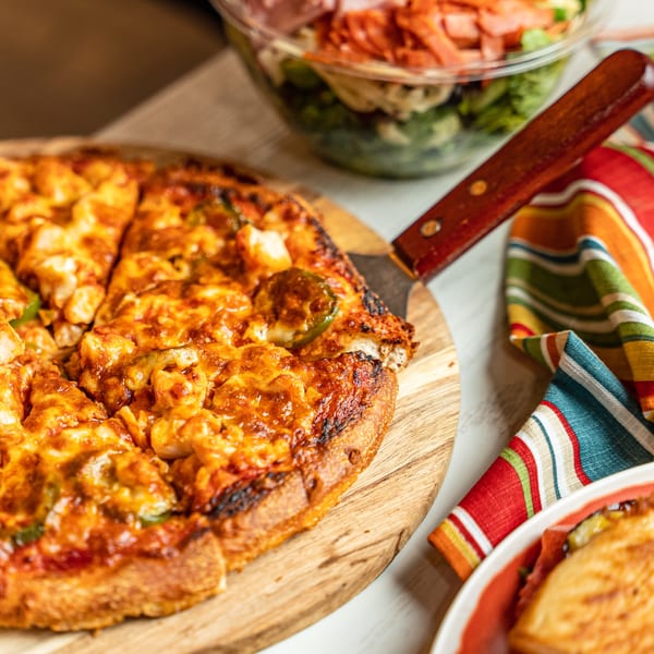 A Singas Famous Pizza with chicken and jalapeños, a salad, and a colorful napkin.