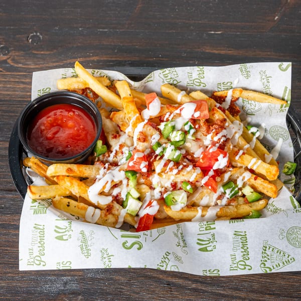 Loaded fries topped with melted cheese, bacon bits, diced tomatoes, jalapeños, and ranch dressing, with a side of ketchup.