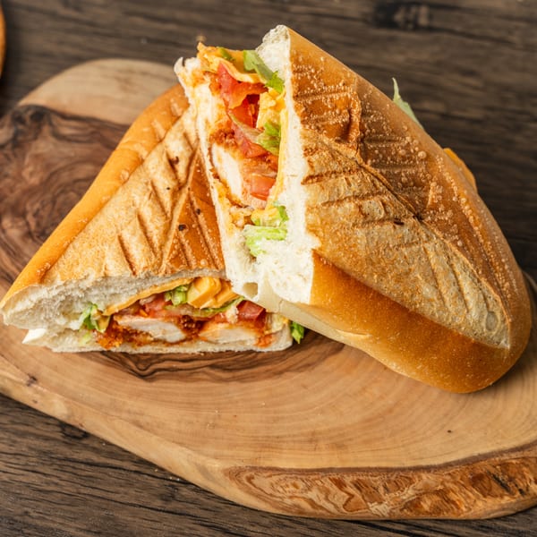 A grilled chicken sandwich with lettuce, tomato, and cheese on a wooden board.