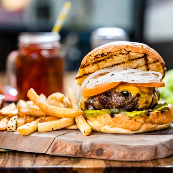Cheeseburger with tomato, onion, and pickles, served with fries and a drink.