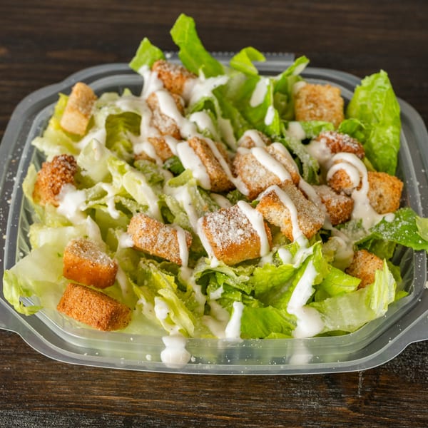 Caesar salad with crisp romaine lettuce, croutons, and creamy dressing in a plastic container.