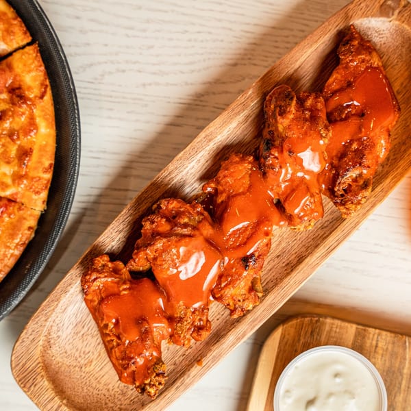 Singas Famous Pizza's buffalo wings covered in hot sauce, with a side of ranch and pizza.