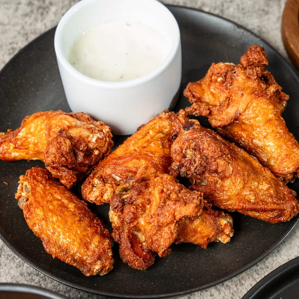 Crispy fried chicken wings on a black plate with a side of ranch dipping sauce.