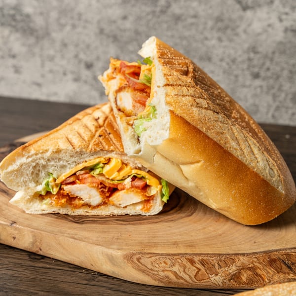 Two halves of a chicken sandwich with lettuce, tomato, and cheese on a wooden board.