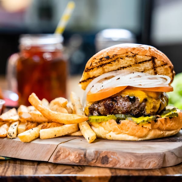 A cheeseburger with fries and a drink on a wooden board, ready to be served at Singas Famous Pizza.