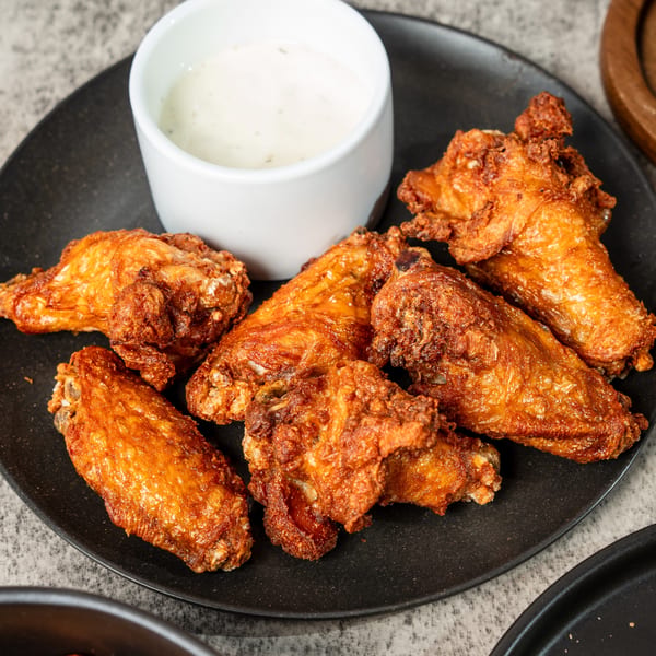 Crispy fried chicken wings on a black plate with a side of ranch dipping sauce.