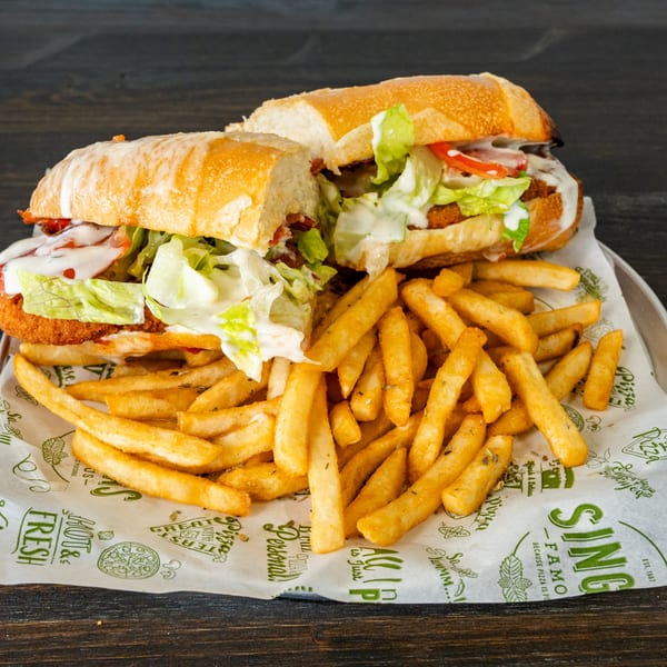 Two chicken sandwiches with lettuce, tomato, and sauce, served with a pile of french fries.