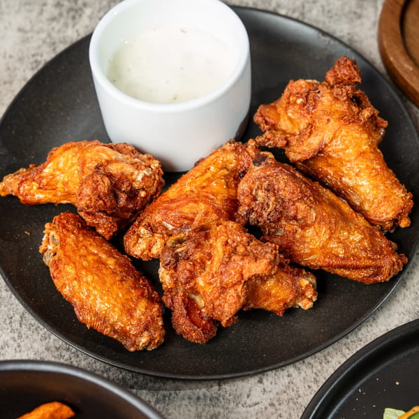 Crispy fried chicken wings on a black plate with a side of white dipping sauce.