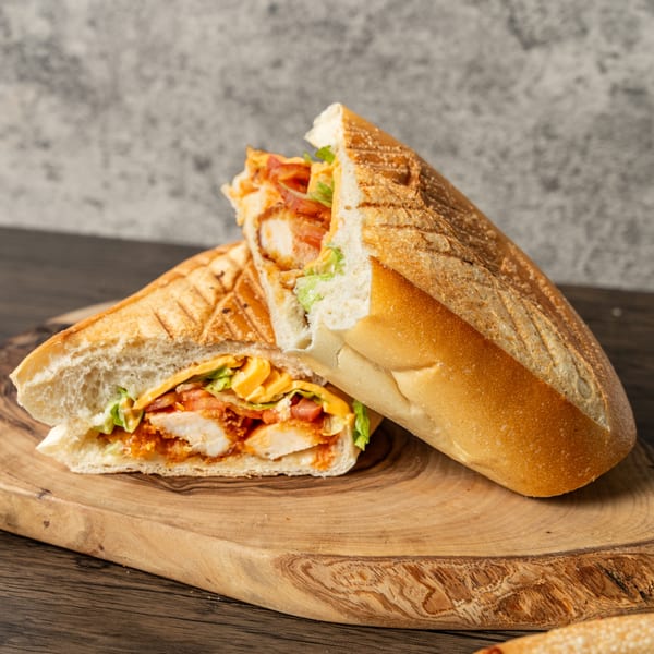 Two halves of a crispy chicken sandwich with cheese, lettuce, and tomatoes on a wooden board.
