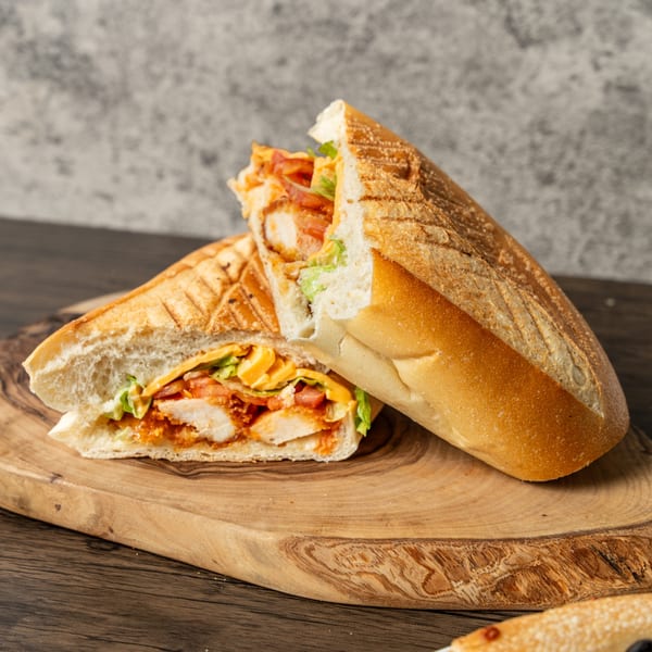 A crispy chicken sandwich, cut in half, with lettuce, tomatoes, and cheese on a wooden board.