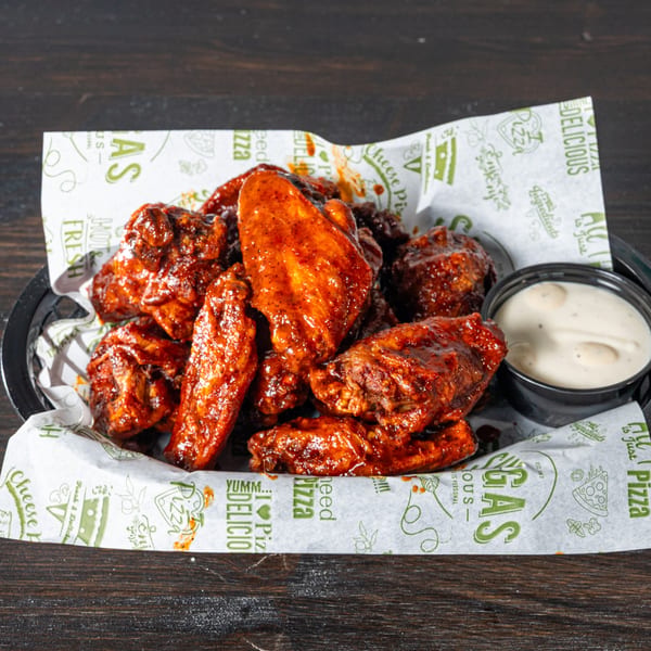 A basket of saucy chicken wings with a side of ranch dressing on a dark wooden table.