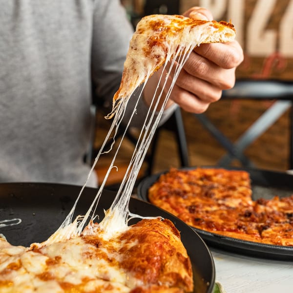 Hand pulling a slice of Singas Famous Pizza, creating long, stretchy cheese strings.