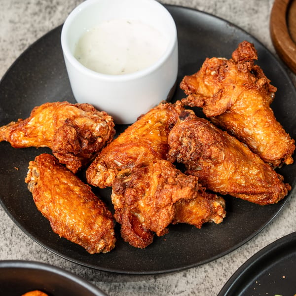 Crispy fried chicken wings on a black plate with a side of ranch dipping sauce.