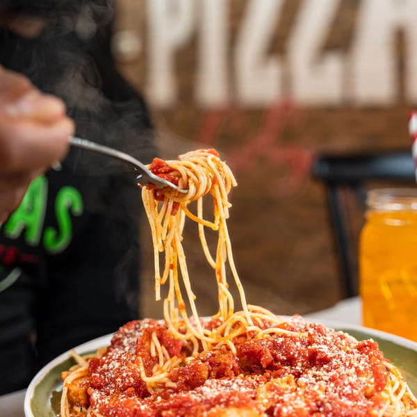 A fork lifts steaming spaghetti with red sauce and parmesan cheese from a plate.