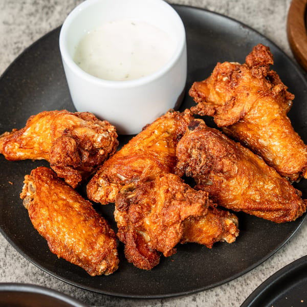 Crispy fried chicken wings on a black plate with a side of creamy dipping sauce.
