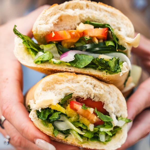Two hands holding two halves of a fresh sandwich filled with lettuce, tomatoes, and onions.