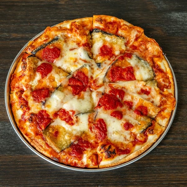A freshly baked eggplant parmesan pizza, cut into slices, in a metal pan on a dark wooden table.