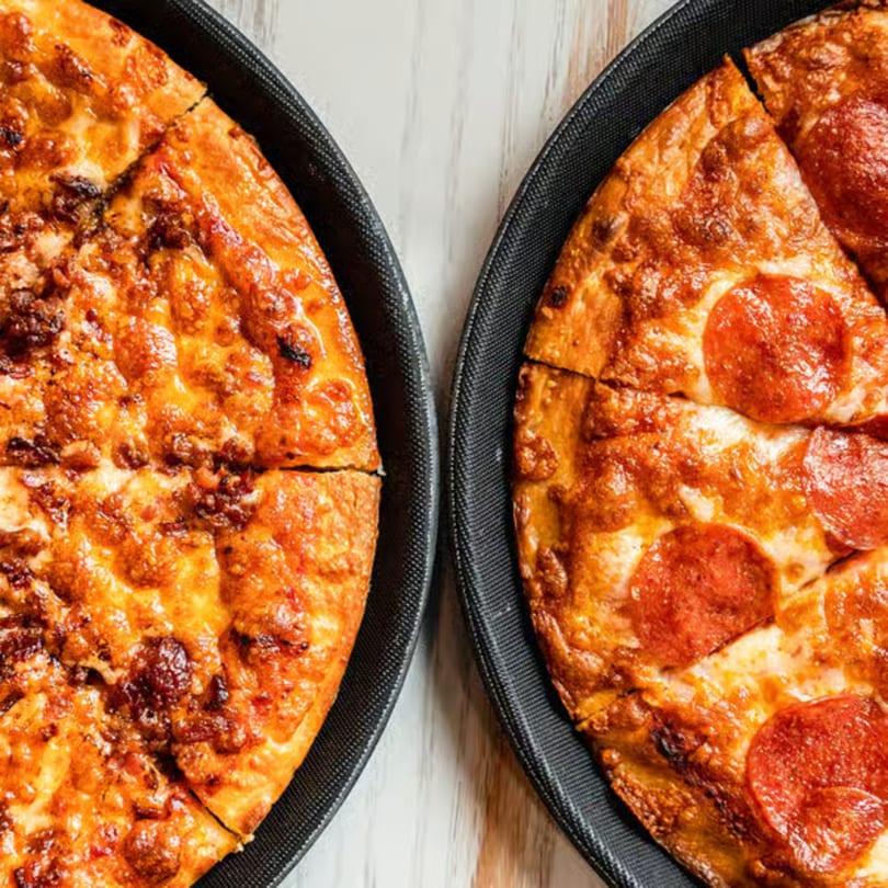 Two Singas Famous Pizzas, one with pepperoni and one with sausage, on black trays.