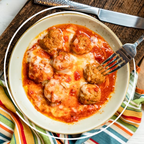 Meatballs in marinara sauce with melted cheese, with a fork, on a colorful striped napkin.