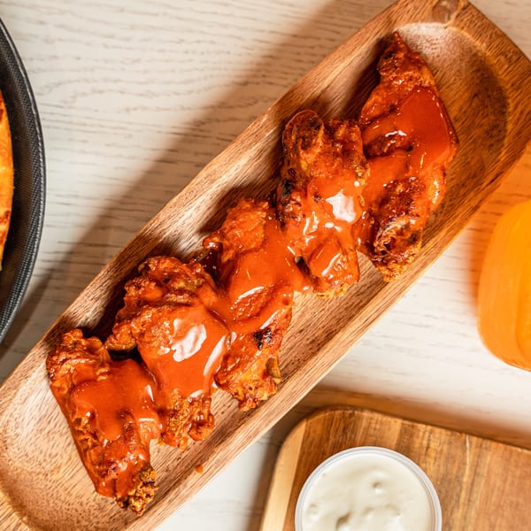 Singas Famous Pizza's buffalo wings, drenched in hot sauce, served on a wooden platter with ranch.