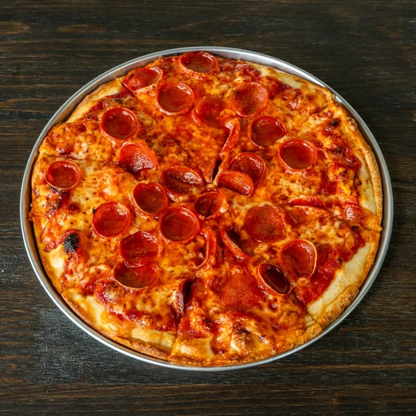 A whole pepperoni pizza in a metal pan, sliced and ready to eat on a dark wooden table.