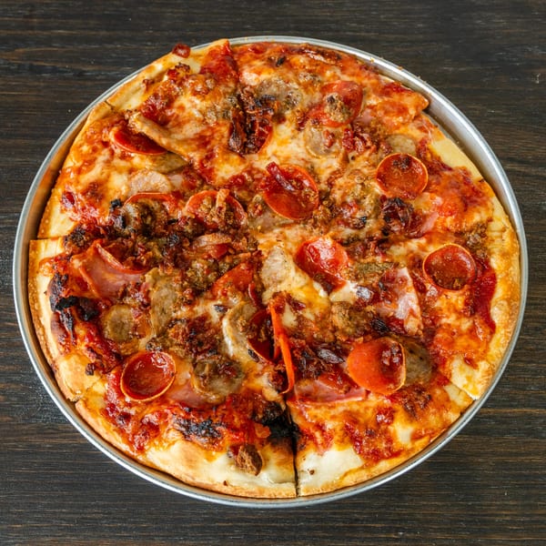 A whole Singas Famous Pizza with pepperoni, sausage, and ham, in a metal pan.