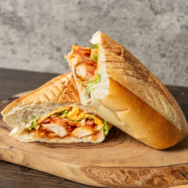 Two halves of a grilled chicken sandwich with cheese, lettuce, and tomatoes on a wooden board.