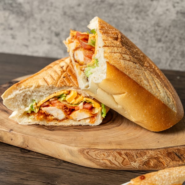 A grilled chicken sandwich, cut in half, filled with cheese, lettuce, and tomatoes on a wooden board.