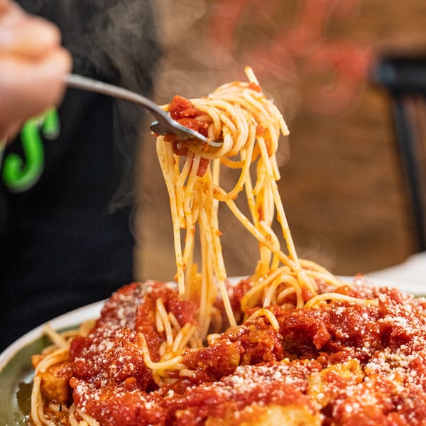 Steaming spaghetti with red sauce and parmesan cheese being lifted by a fork.