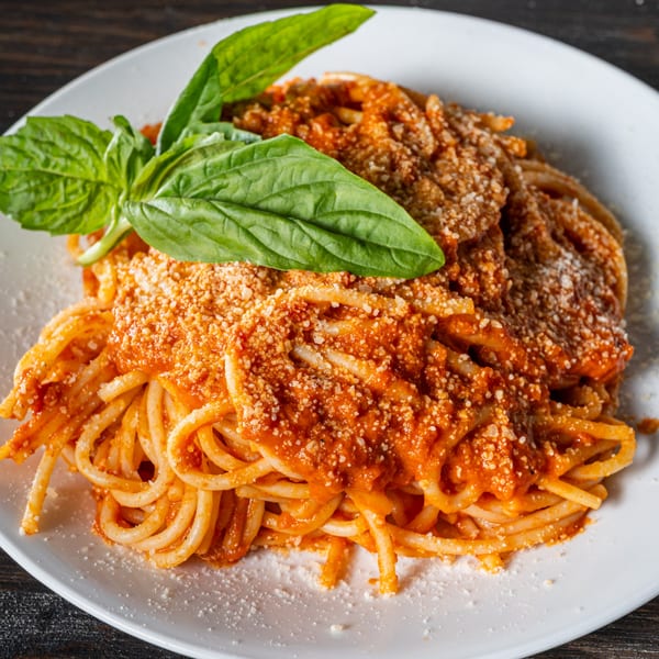 Close-up of spaghetti with red sauce, grated cheese, and a fresh basil garnish on a white plate.