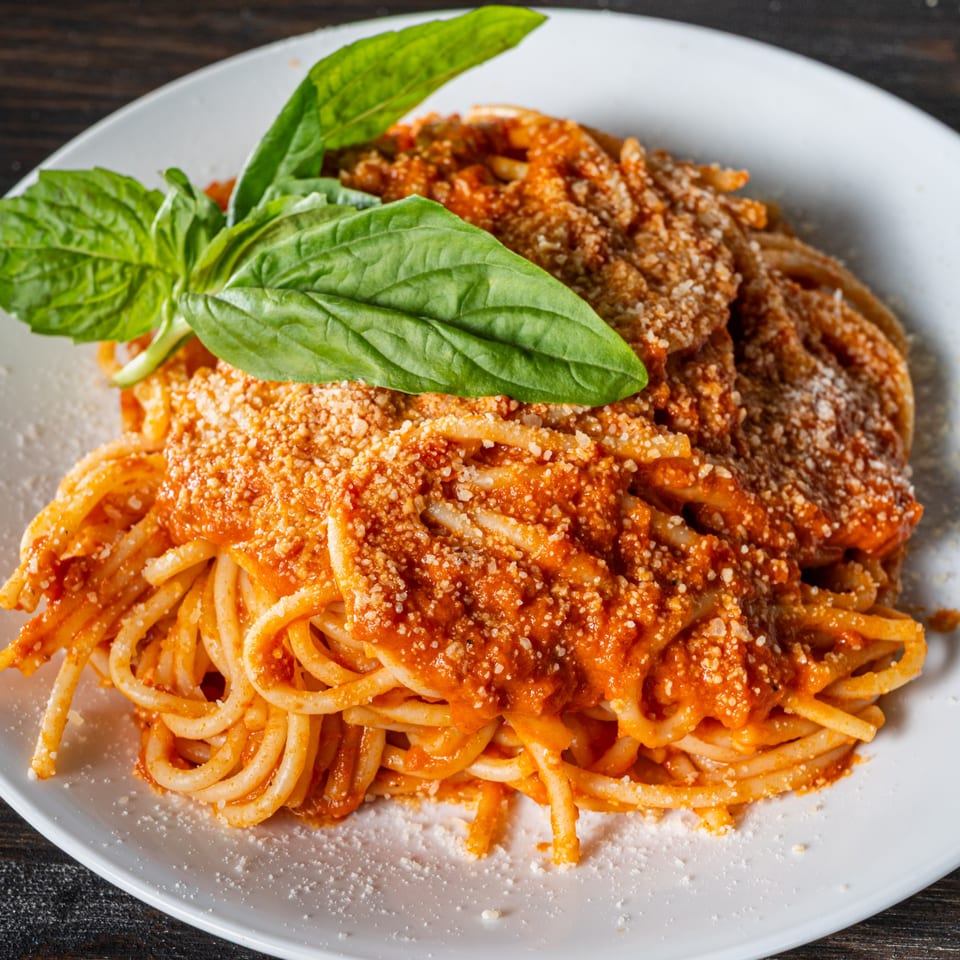Close-up of spaghetti with red sauce, grated cheese, and a fresh basil garnish on a white plate.