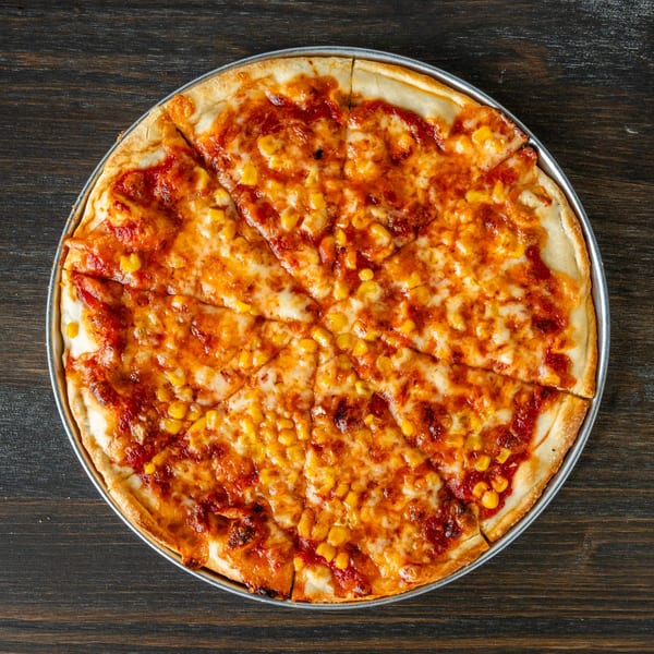 A whole Singas Famous Pizza with corn and cheese, sliced into eight pieces on a dark wooden table.
