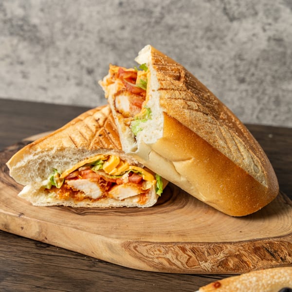A toasted chicken sandwich, cut in half, filled with lettuce, tomatoes, and cheese on a wooden board.