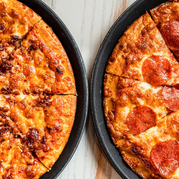 Two Singas Famous Pizzas, one with pepperoni and one with ground meat, on black trays.