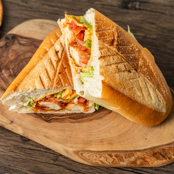 Two halves of a grilled chicken sandwich with lettuce, tomato, and cheese on a wooden board.