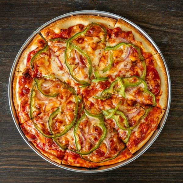 A whole Singas Famous Pizza with green peppers and red onions, sliced into eight pieces.