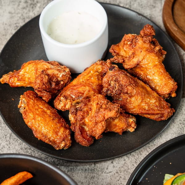 Crispy fried chicken wings on a black plate with a side of ranch dipping sauce.