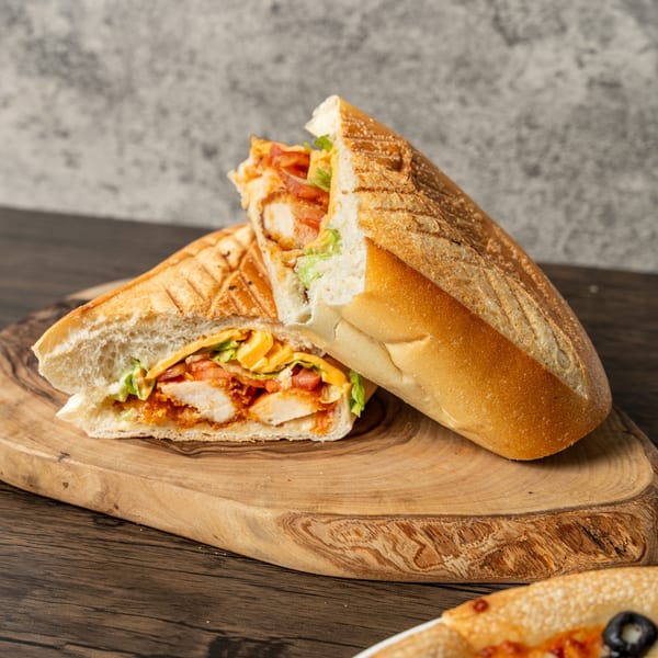 A toasted chicken panini sandwich, cut in half, revealing chicken, cheese, lettuce, and tomato.