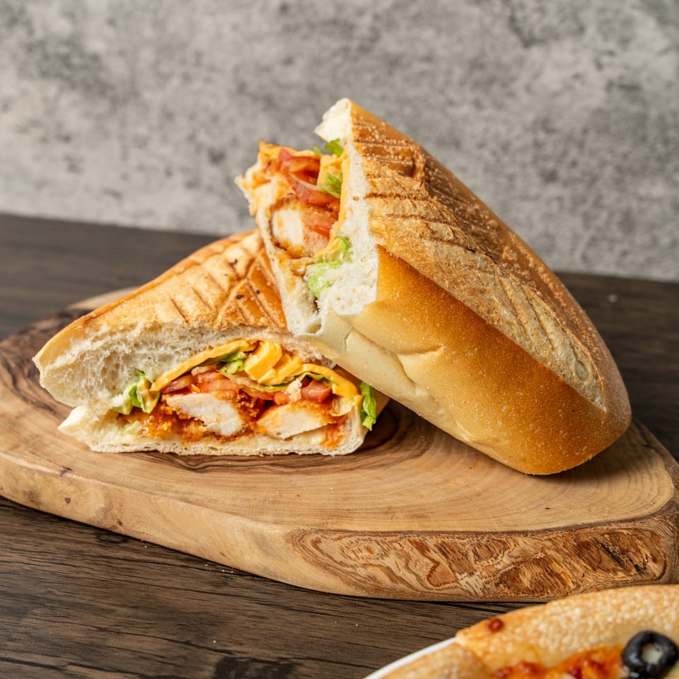 A toasted chicken panini sandwich, cut in half, revealing chicken, cheese, lettuce, and tomato.