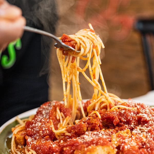 Steaming spaghetti with red sauce and parmesan cheese being twirled onto a fork.
